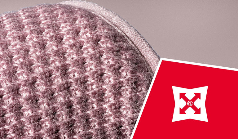 Gros plan sur un tissu en laine tricotée rose et grise, montrant la texture et les mailles détaillées. Une icône rouge représente un bouclier blanc avec des flèches, symbolisant la durabilité ou la résistance.