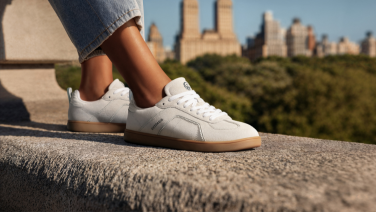 Baskets blanches aux pieds d'une personne en pantalon foncé, assise sur un mur, avec la silhouette d'une ville en arrière-plan