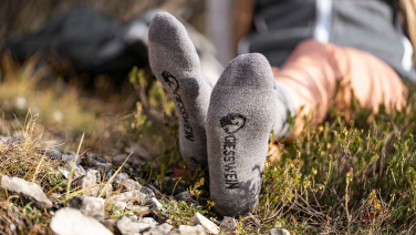 Gros plan sur des plantes de pieds chaussées de chaussettes Giesswein grises avec logo noir, dans un pré.