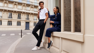 Un homme en pantalon noir et chemise blanche et une femme en tailleur-pantalon bleu sont appuyés contre le rebord de la fenêtre.