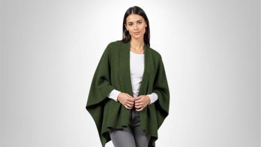 Femme portant un poncho en laine mérinos vert foncé sur un t-shirt blanc et un jean gris devant un fond gris clair
