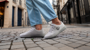 Détail : pieds chaussés de baskets Giesswein Merino Wool gris clair sur les pavés historiques d'une ruelle méditerranéenne dans la vieille ville.