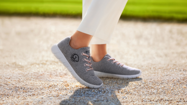 Vue latérale d'une personne en pantalon blanc et baskets Giesswein Merino grises sur un chemin de gravier à l'extérieur