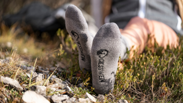 Une personne est allongée dans un pré ; au premier plan, on aperçoit ses pieds chaussés de chaussettes grises ornées d'un logo.