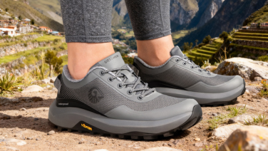 Gros plan sur des chaussures de randonnée Giesswein grises dotées d'une membrane imperméable aux pieds d'une femme ; en arrière-plan, un paysage montagneux rocheux avec des champs en terrasses au Pérou.