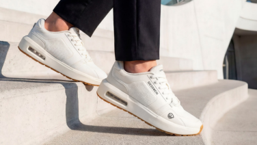 Gros plan sur des baskets blanches Giesswein dotées d'une semelle à coussin d'air apparente et d'un pantalon noir, alors que la personne monte un escalier en pierre claire.