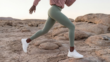 Une femme courant sur un sol rocailleux, visible de la taille aux pieds. Elle porte un legging vert menthe, on aperçoit une manche rose pâle en haut de l'image, et aux pieds, des baskets blanches Giesswein.