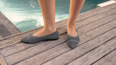  Gros plan sur deux pieds chaussés de ballerines en tricot gris, posés sur une passerelle en bois au bord de la piscine.