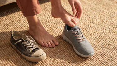 Une personne enfile une basket grise « Giesswein Merino » sur un tapis en sisal ; à côté se trouve une vieille chaussure usée.