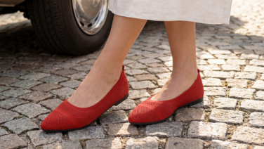 Gros plan sur des pieds en train de marcher, chaussés de ballerines en maille rouge Giesswein ornées d'un motif à rayures texturées, sur un pavé.