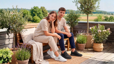 Deux personnes sont assises sur un banc en bois, sur une terrasse agrémentée de lavande et de plantes en pot ; elles portent des baskets Giesswein Merino Runner blanches et noires.