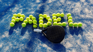 Une raquette de padel noire repose sur un court en dur bleu. Des balles de tennis jaune-vert sont disposées à côté, formant le mot « PADEL ».