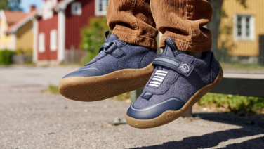 Gros plan sur les pieds d'un enfant en pantalon en velours côtelé marron, qui pendent dans le vide. Il porte des chaussures pour enfant en laine mérinos bleu foncé.