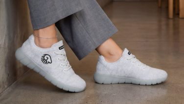 Gros plan sur des jambes féminines vêtues d'un pantalon gris et de baskets en laine mérinos blanc crème de la marque Giesswein, sur un sol en béton.