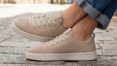 Gros plan sur une basket Giesswein couleur sable, dotée d'une tige en tricot texturé et d'une semelle blanche. La personne porte un jean clair et est assise sur un pavé.