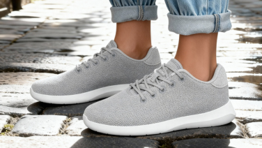 Gros plan sur des baskets Giesswein Merino gris clair à semelle blanche sur des pavés, portées avec un jean retroussé, sous la lumière du soleil.