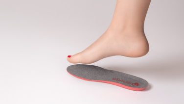 Un pied nu avec du vernis à ongles rouge flotte au-dessus d'une semelle intérieure Giesswein grise à bord rouge sur fond blanc.
