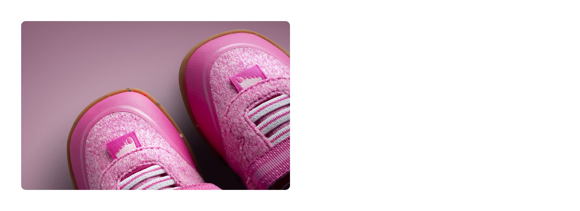 Gros plan sur deux chaussures pour enfants Giesswein de couleur rose, avec une tige en laine mérinos, des lacets élastiques et une semelle couleur miel, sur fond rose.